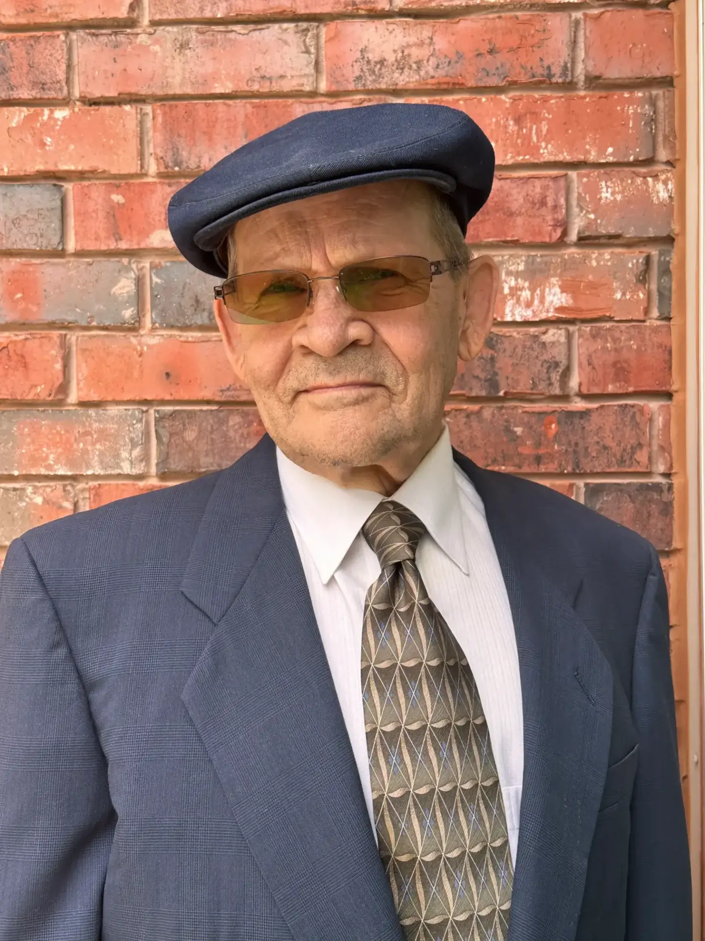 Elderly man in suit and cap.